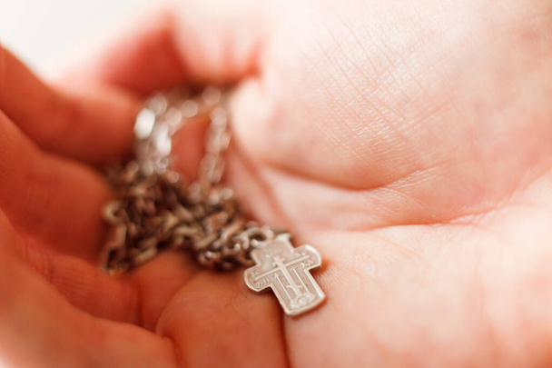 Silver cross in the hand with focus on the cross, shallow DOF - Foto, afbeelding
