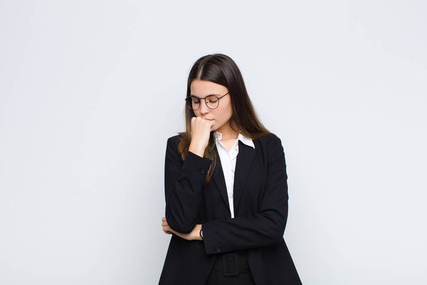 young businesswoman feeling serious, thoughtful and concerned, staring sideways with hand pressed against chin against white wall - Fotoğraf, Görsel