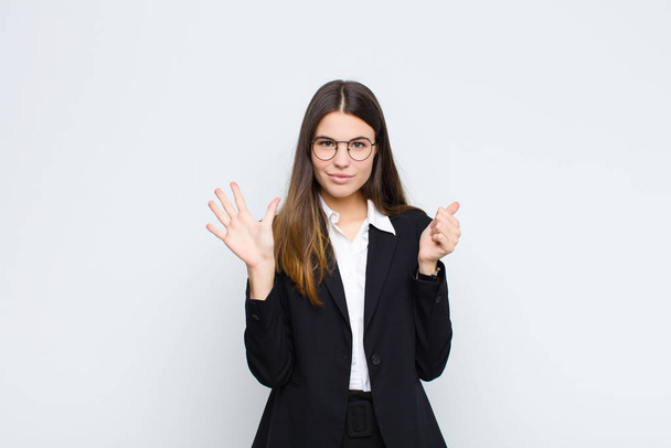 young businesswoman smiling and looking friendly, showing number six or sixth with hand forward, counting down against white wall - Fotoğraf, Görsel