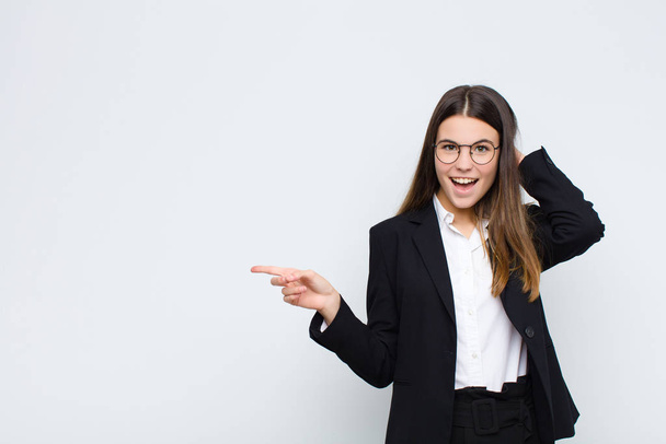 young businesswoman laughing, looking happy, positive and surprised, realizing a great idea pointing to lateral copy space against white wall - Foto, Bild