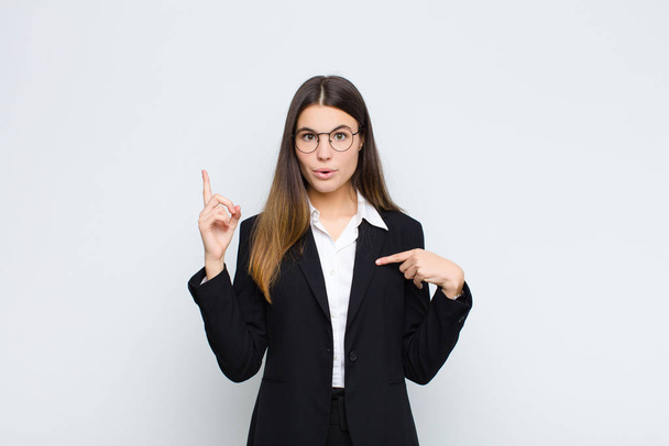 young businesswoman feeling proud and surprised, pointing to self confidently, feeling like successful number one against white wall - Fotoğraf, Görsel