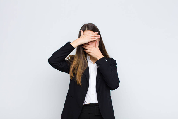 young businesswoman covering face with both hands saying no to the camera! refusing pictures or forbidding photos against white wall - 写真・画像