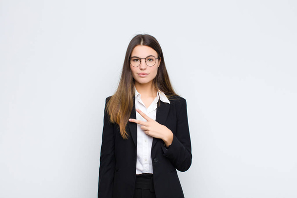 young businesswoman feeling happy, positive and successful, with hand making v shape over chest, showing victory or peace against white wall - Photo, image