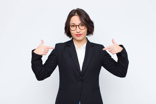 young businesswoman looking proud, positive and casual pointing to chest with both hands against white wall - Foto, Bild