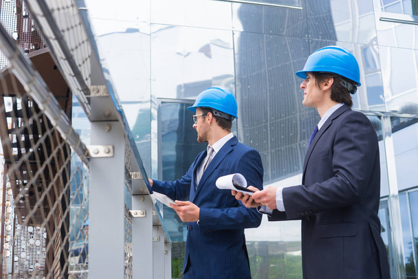 Real estate developers in helmets. New office construction. Confident business men and architect talking in front of modern office building. Businessman and his colleague have conversation. - Φωτογραφία, εικόνα