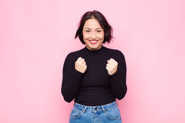 young pretty woman shouting triumphantly, laughing and feeling happy and excited while celebrating success against pink wall - Fotoğraf, Görsel