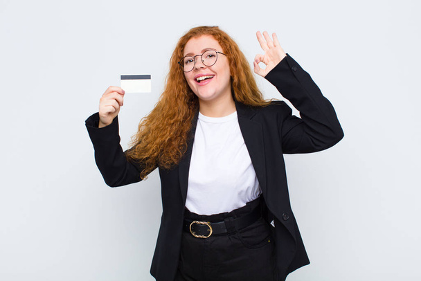 red head young woman feeling happy, relaxed and satisfied, showing approval with okay gesture, smiling against white wall - Foto, afbeelding