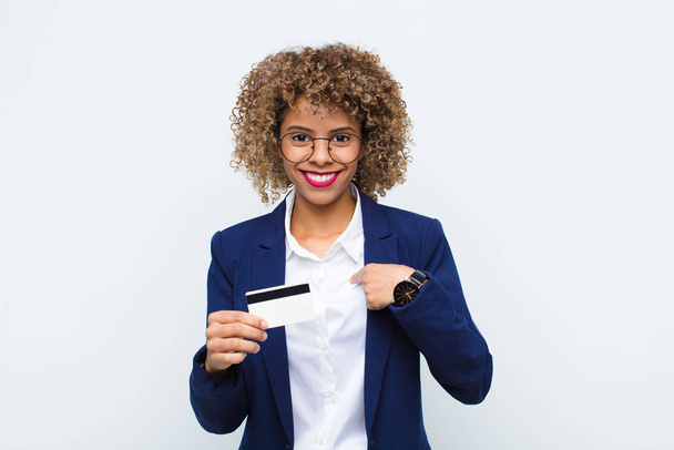 young african american woman feeling happy, surprised and proud, pointing to self with an excited, amazed look with a credit card - Photo, Image