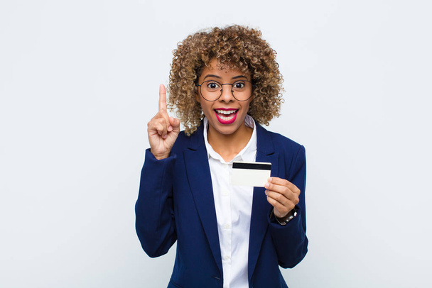 young african american woman feeling like a happy and excited genius after realizing an idea, cheerfully raising finger, eureka! with a credit card - Фото, изображение