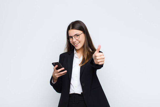 young pretty woman feeling proud, carefree, confident and happy, smiling positively with thumbs up with a mobile phone - Photo, image