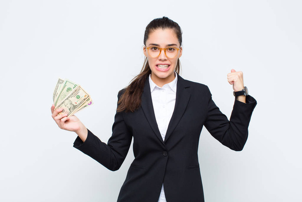 young businesswoman shouting aggressively with an angry expression or with fists clenched celebrating success with banknotes with bills - Фото, зображення