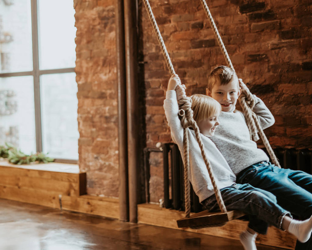 two boys swinging on a swing indoor. happy children. place for text - 写真・画像