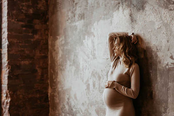 Красива вагітна дівчина 29 тижня в студії. сім місяців вагітна дівчина в бежевій сукні позує на фотосесії. стильна вагітна жінка. мати бути
. - Фото, зображення