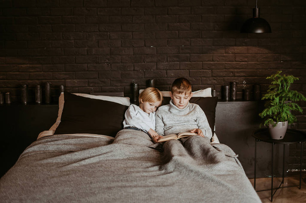 Two sweet boys, reading a book in bed after bedtime. Cute children reading book on bed, vintage filter. loft interior - Foto, imagen