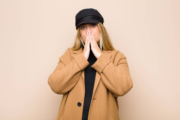 young blonde woman happy and excited, surprised and amazed covering mouth with hands, giggling with a cute expression against flat wall - Photo, Image