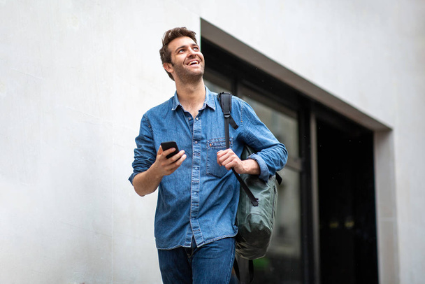 Portré boldog idősebb férfi séta mobiltelefon és táska pin város - Fotó, kép