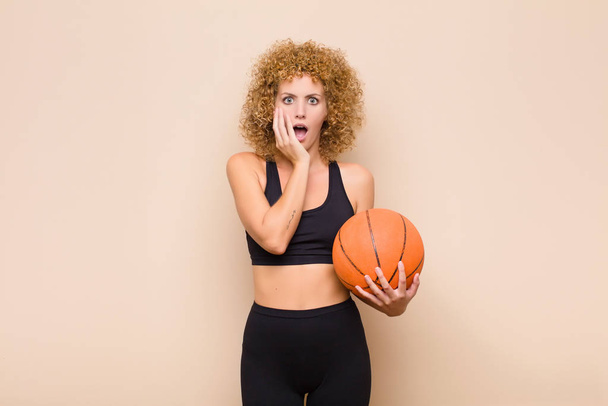 young afro woman open-mouthed in shock and disbelief, with hand on cheek and arm crossed, feeling stupefied and amazed sport concept - Photo, image
