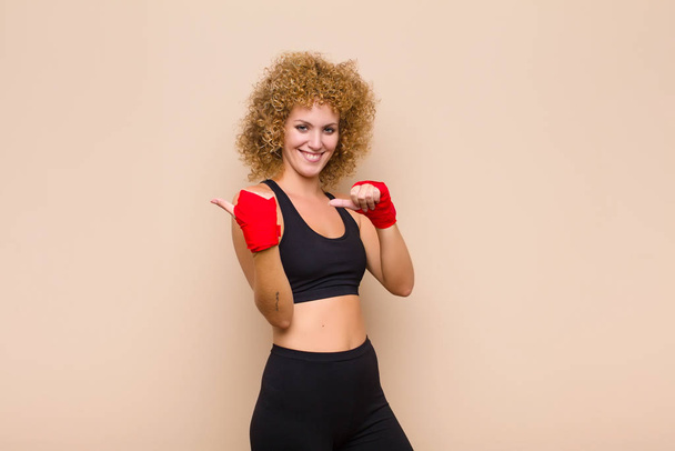 young afro woman smiling cheerfully and casually pointing to copy space on the side, feeling happy and satisfied sport concept - Foto, Imagem