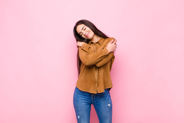 young pretty woman feeling in love, smiling, cuddling and hugging self, staying single, being selfish and egocentric against pink wall - Fotografie, Obrázek