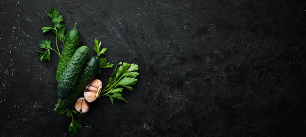 Cucumber and garlic on a black stone background. Top view. Free space for your text. - Fotó, kép