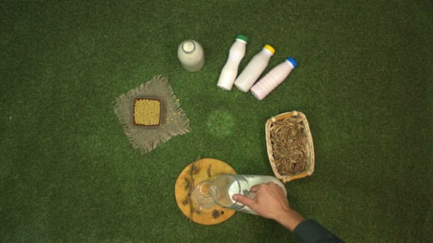 Soy milk. Slow motion 2x. Top view.Soy milk and dairy products from soy on the lawn.The male hand takes a jug and pours milk into a mug.The other hand takes the mug and after a short time puts it back on the grass. - Footage, Video