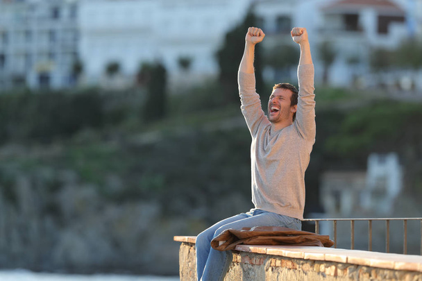 Excited man raising arms celebrating success in a balcony - Φωτογραφία, εικόνα