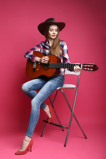 Jonge vrouw met cowboy hoed en gitaar op een roze achtergrond - Foto, afbeelding