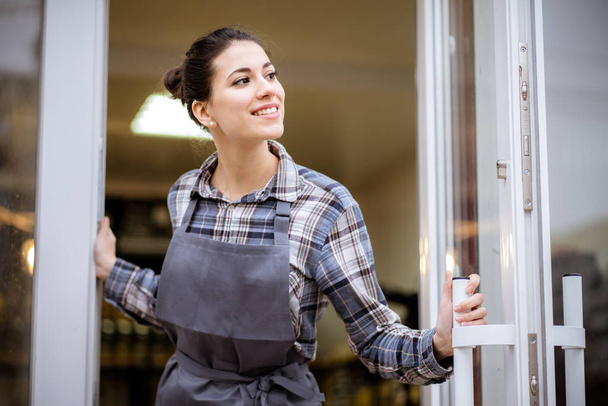 Piękna azjatycka kobieta właścicielka sklepu ze stojącym w drzwiach kawiarni patrząc w kamerę i uśmiechając się.Portret kelnerki w fartuchu i stojącej z przodu - Zdjęcie, obraz