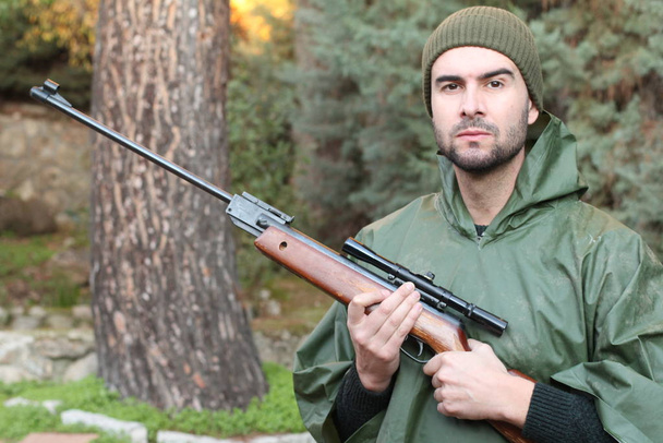 Außenporträt eines jungen Jägers, der mit Gewehr im Wald steht - Foto, Bild