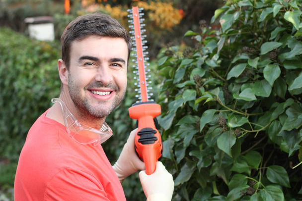 retrato cercano de un joven guapo con vigas eléctricas cortando arbustos en el jardín. - Foto, imagen