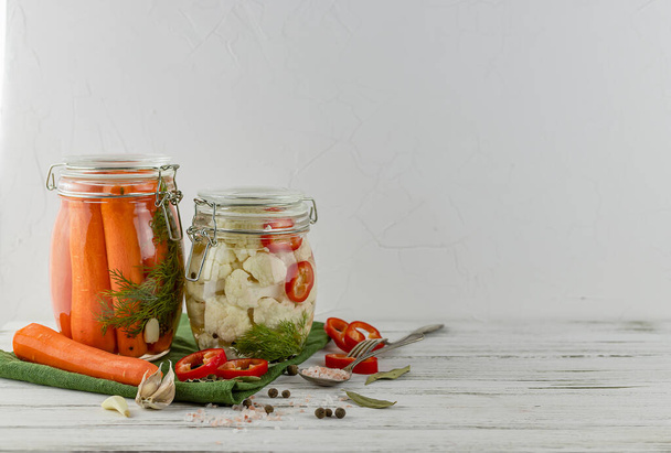 dwa szklane słoiki sfermentowanego kalafiora, marchewka. warzywa na jasnym tle. przy użyciu tekstyliów jasnoszary. fermentacja jest źródłem probiotyku. przestrzeń kopiowania - Zdjęcie, obraz