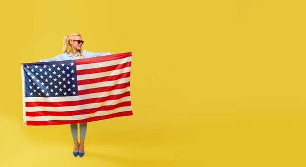 American girl. Happy young woman in denim clothes holding USA flag isolated on yellow background. Banner. Copy space for text - Fotoğraf, Görsel