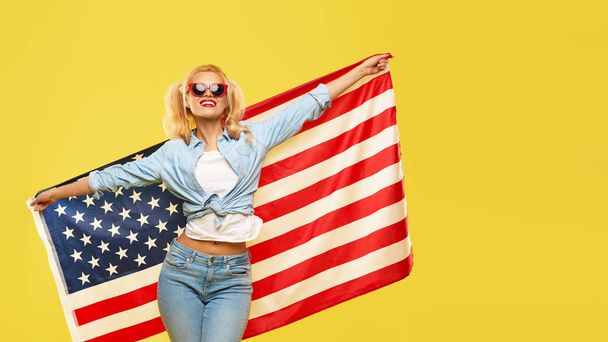 American girl. Happy young woman in denim clothes holding USA flag isolated on yellow background - Photo, Image