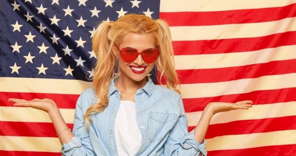 American girl. Happy young woman in heart shape sunglasses on USA flag  background. Funny and surprised human face. Patriotism concept - Fotoğraf, Görsel