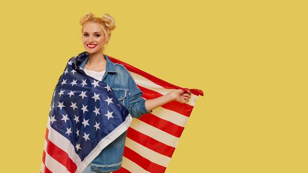 American girl. Happy young woman in denim clothes holding USA flag isolated on yellow background. Banner. Empty space for text - Foto, Imagem