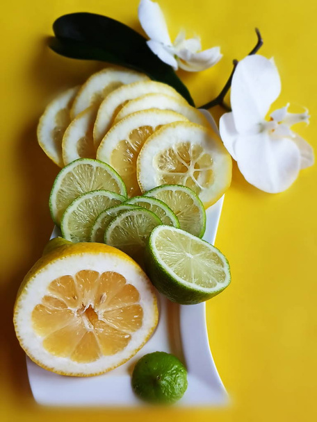 Λεμόνι φέτες εσπεριδοειδών και ασβέστη εσπεριδοειδών ζουμερό φέτα φρούτων σε μπλε πιάτο φόντο νεκρή φύση, υγιεινά τρόφιμα και vitamiin με ορχιδέες λουλούδια, πράσινο και κίτρινο διακόσμηση τροφίμων  - Φωτογραφία, εικόνα