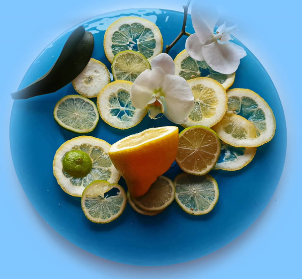 Citron tranches agrumes et citron vert agrumes tranche juteuse fruits sur fond plat bleu nature morte, nourriture saine et vitamiine avec des fleurs d'orchidées, vert et jaune décoration alimentaire design
  - Photo, image