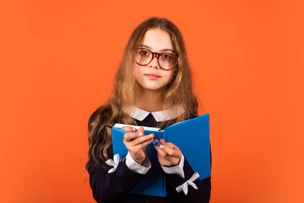 Always beautiful and smart every moment. Smart girl hold book and pen brown background. Small child with smart look in glasses. School and education. Private teaching. Smart and genius - Valokuva, kuva