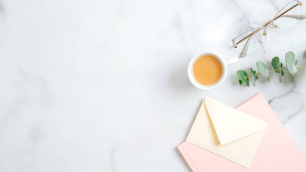 Feminine workspace with cup of coffee, glasses, pink paper notebook and envelope with love letter on marble background. Flat lay, top view, copy space. Wedding, bridal, marriage concept. - Φωτογραφία, εικόνα