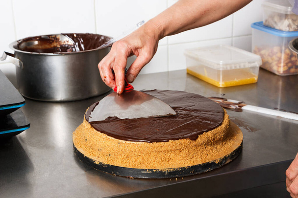 Mulher esfrega bolo de chocolate com cobertura de gelo, fase final da culinária. Feito por mãos para confeitaria
. - Foto, Imagem