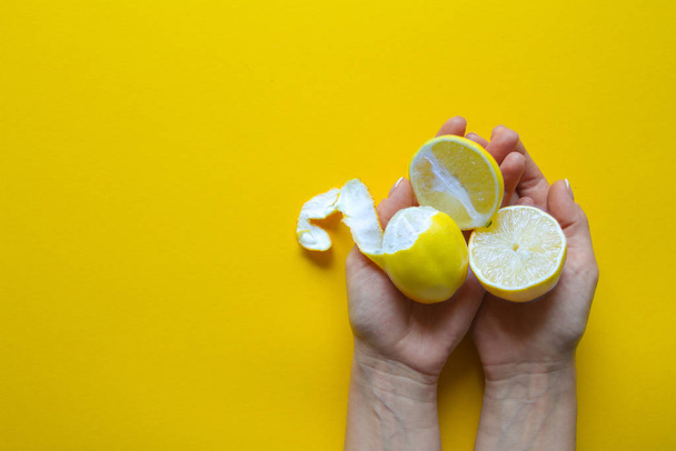 Κάτοψη των γυναικείων χεριών που κρατούν ολόκληρα και κομμένα σε φέτες ώριμα λεμόνια σε κίτρινη επιφάνεια, έννοια της υγείας και των βιταμινών - Φωτογραφία, εικόνα