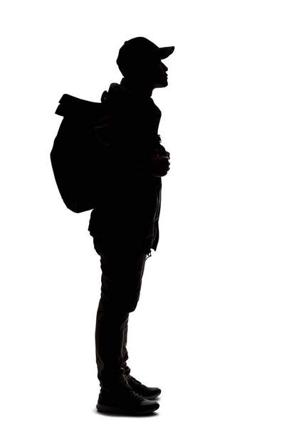 Silhouette of a man hiking and carrying a backpack on a white background.  The isolated side view man can be used for composites.  Depicts adventure and exploration.  - Фото, изображение