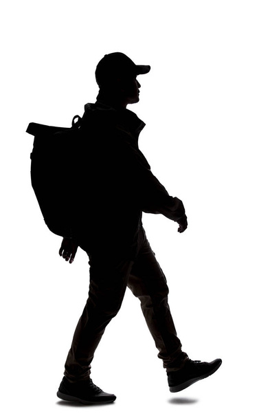 Silhouette of a man wearing a backpack looking like a traveler or hiker trekking. He is walking or hiking  - Fotó, kép