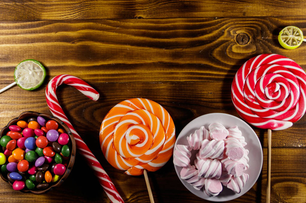 Colorful chocolate candies, lollipops, candy cane and marshmallows on wooden table - Фото, зображення