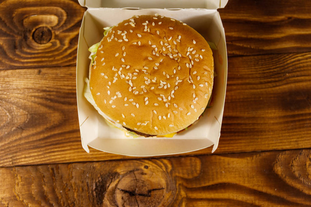 Ahşap masa üzerinde karton kutu içinde lezzetli büyük hamburger - Fotoğraf, Görsel