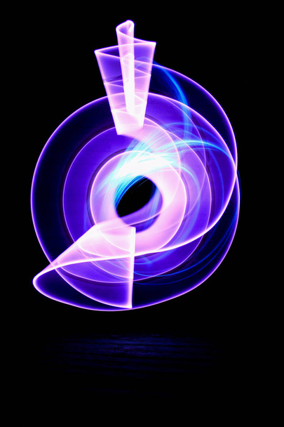 Вигнуті абстрактні форми з фіолетового світлого шабля на фоні. Сеанс світлового живопису у довгому експозиції вночі
. - Фото, зображення