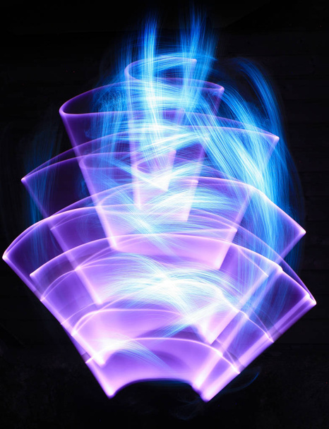 Zakrzywione abstrakcyjne kształty wykonane z fioletowego miecza świetlnego w tle. Sesja Lightpainting w długiej ekspozycji w nocy. - Zdjęcie, obraz