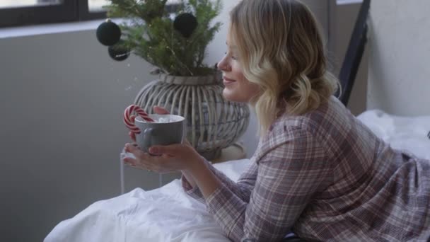 Hermosa mujer en pijama se acuesta en la cama y sostiene una gran taza con cacao, ambiente acogedor en casa, cálida noche de invierno en casa, Full HD 120 fps Prores HQ
 - Metraje, vídeo