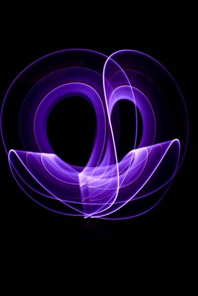 Вигнуті абстрактні форми з фіолетового світлого шабля на фоні. Сеанс світлового живопису у довгому експозиції вночі
. - Фото, зображення
