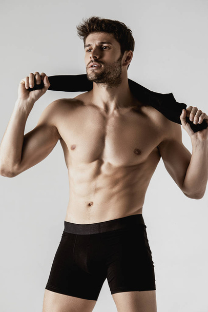 Ισχυρή απογυμνωμένο αρσενικό μοντέλο μυών σε μαύρο εσώρουχο και μαύρες μακριές κάλτσες σε γκρι απομονωμένο φόντο γραμματοσειράς - Φωτογραφία, εικόνα